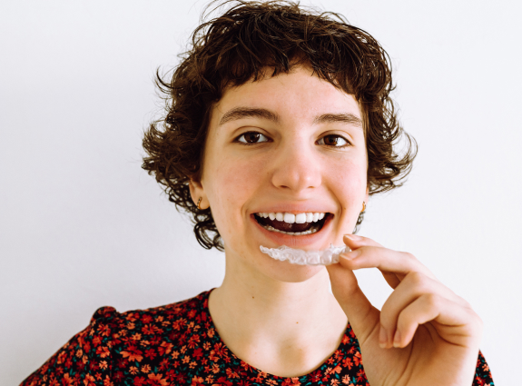Young woman smiling while brushing teeth against white background for orthodontics website