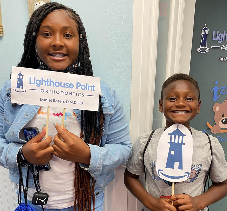 Two children smiling while holding Lighthouse Point Orthodontics promotional materials in an orthodontic office.