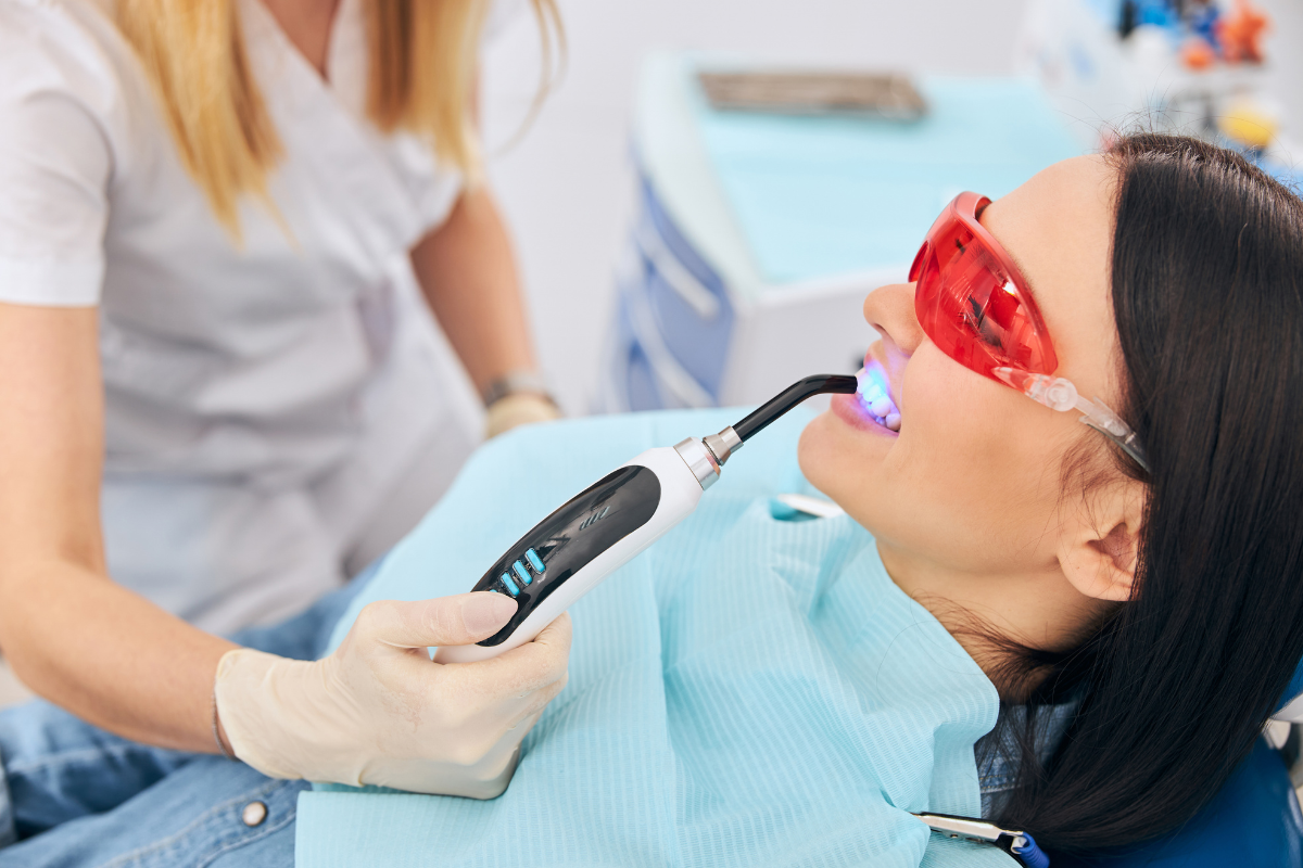 Dentist using UV light technology to whiten patient's teeth during professional dental treatment.